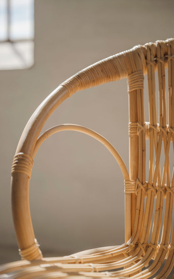 Dies ist ein Nahaufnahmebild von Robert Esszimmerstuhl in polished natural rattan. Geschwungene Armlehne und umwickelte Rattandetails.