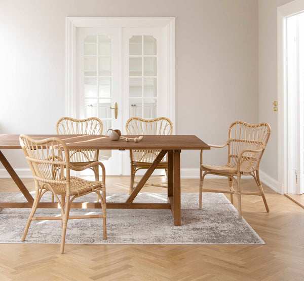 Dies ist ein Lifestyle-Bild von Margret Esszimmerstuhl in natural rattan. Platziert um einen Teak-Esstisch in einem hellen skandinavischen Raum mit Eichenholzboden.