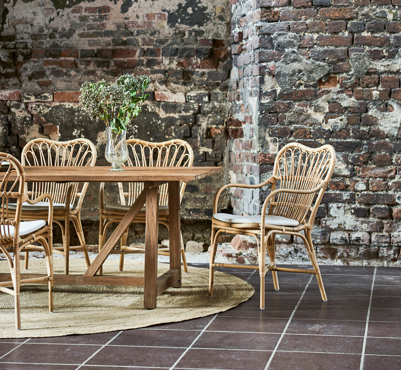 Dies ist ein Lifestyle-Bild von Margret Esszimmerstuhl in natural rattan. Industrielles Loft mit freiliegender Backsteinwand und Juteteppich.