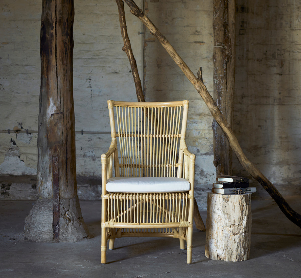 Dies ist ein Lifestyle-Bild von Davinci Esszimmerstuhl in natural rattan, in einem hellen Interieur mit weißen Wandpaneelen und Fischgrätparkett.