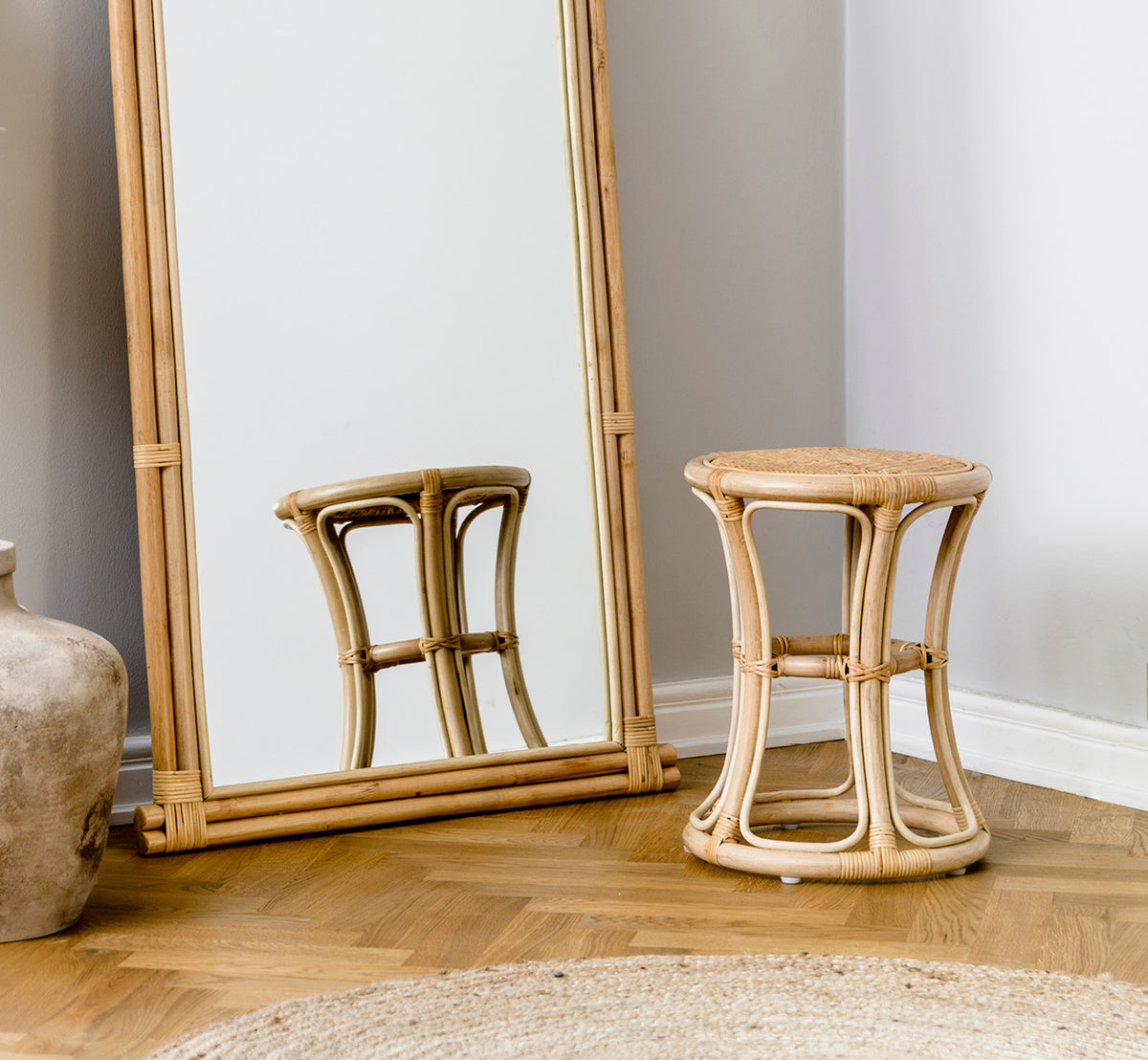 Dies ist ein Lifestyle-Bild von Bella Hocker in natural rattan, in einem hellen Interieur mit weißen Wandpaneelen und Fischgrätparkett.