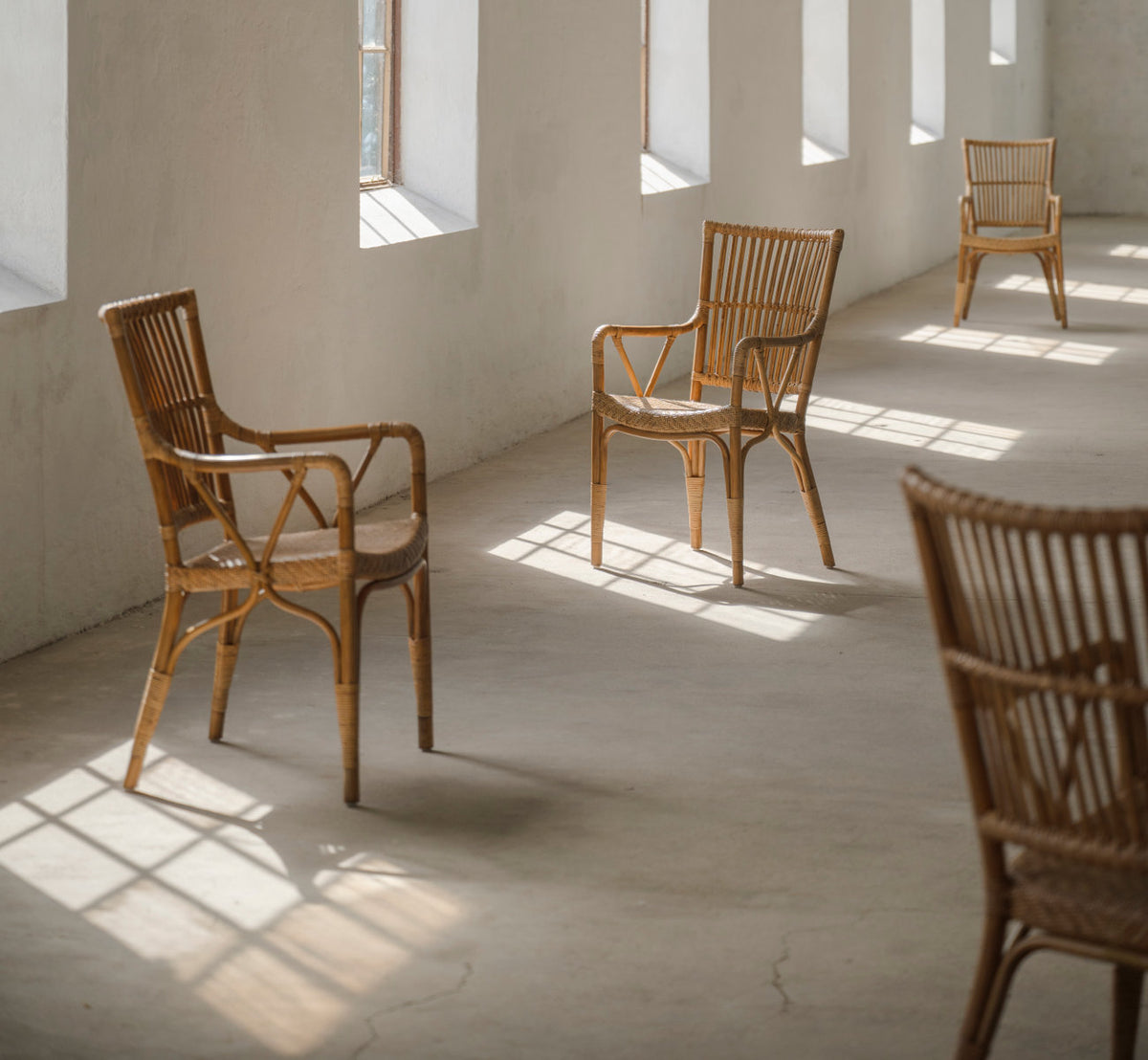 Dies ist ein Lifestyle-Bild von Piano Esszimmerstuhl in antique rattan. Stühle in einem sonnigen Raum mit Betonboden.