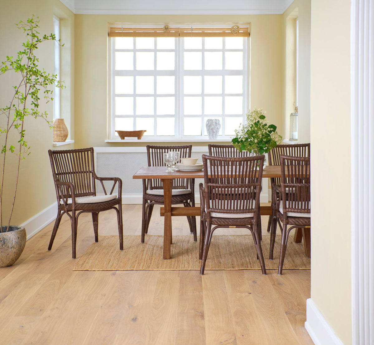 Dies ist ein Lifestyle-Bild von Piano Esszimmerstuhl in brown rattan. Um einen Teak-Esstisch am Fenster.