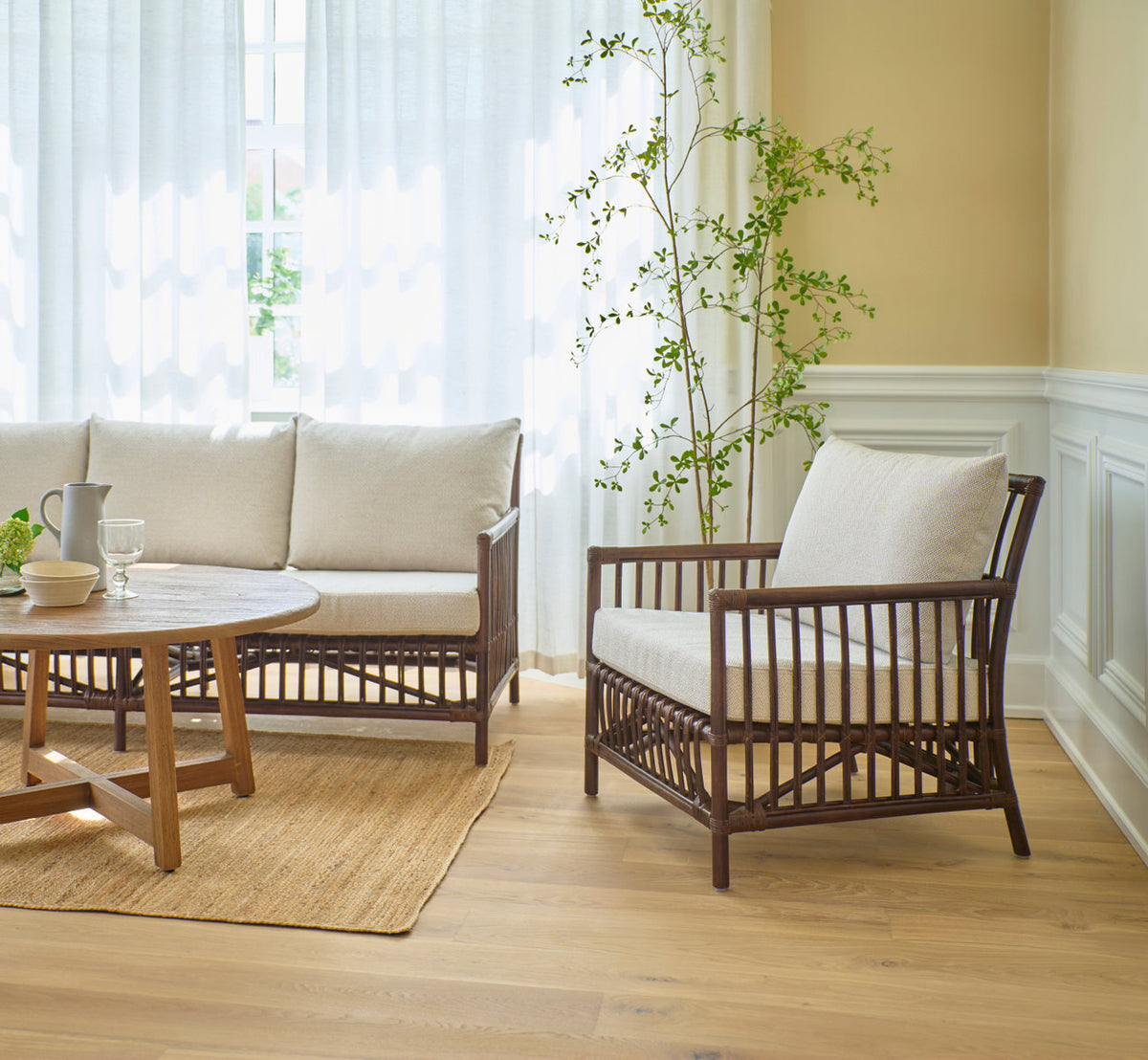 Dies ist ein Lifestyle-Bild von Caroline Lounge-Sessel in brown rattan. Mit Sofa und Teak-Couchtisch in einem hellen Wohnzimmer.
