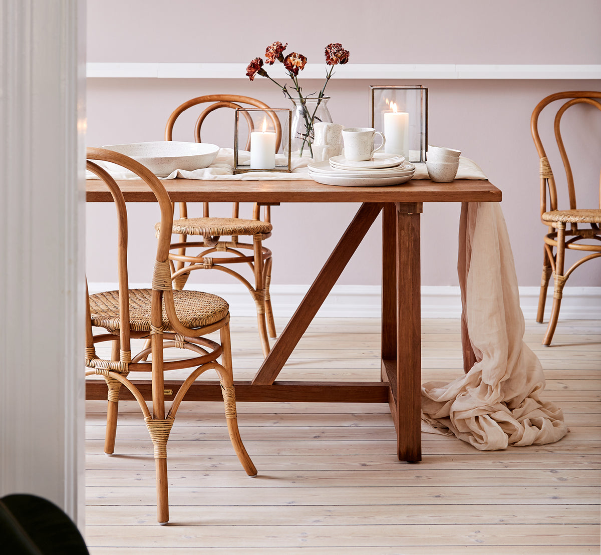 Dies ist ein Lifestyle-Bild von Lulu Esszimmerstuhl in antique rattan. An einem Teak-Esstisch mit Kerzen und Leinen in einem warmtonigen Interieur gestylt.