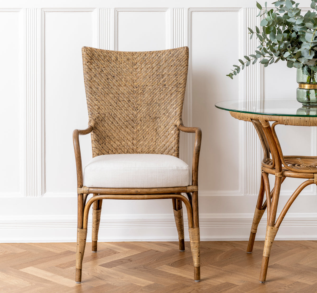 Dies ist ein Lifestyle-Bild von Melody Dining Armchair i antique rattan. An einem weißen Esstisch in einem hellen skandinavischen Raum.