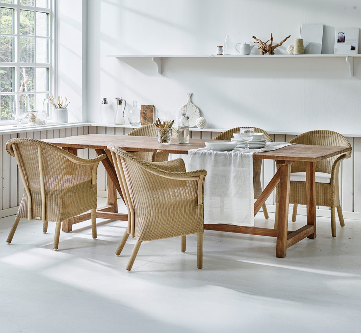 Dies ist ein Lifestyle-Bild von Classic Esszimmerstuhl in natural Loom Rattan Frame, in einem hellen Interieur mit weißen Wandpaneelen und.
