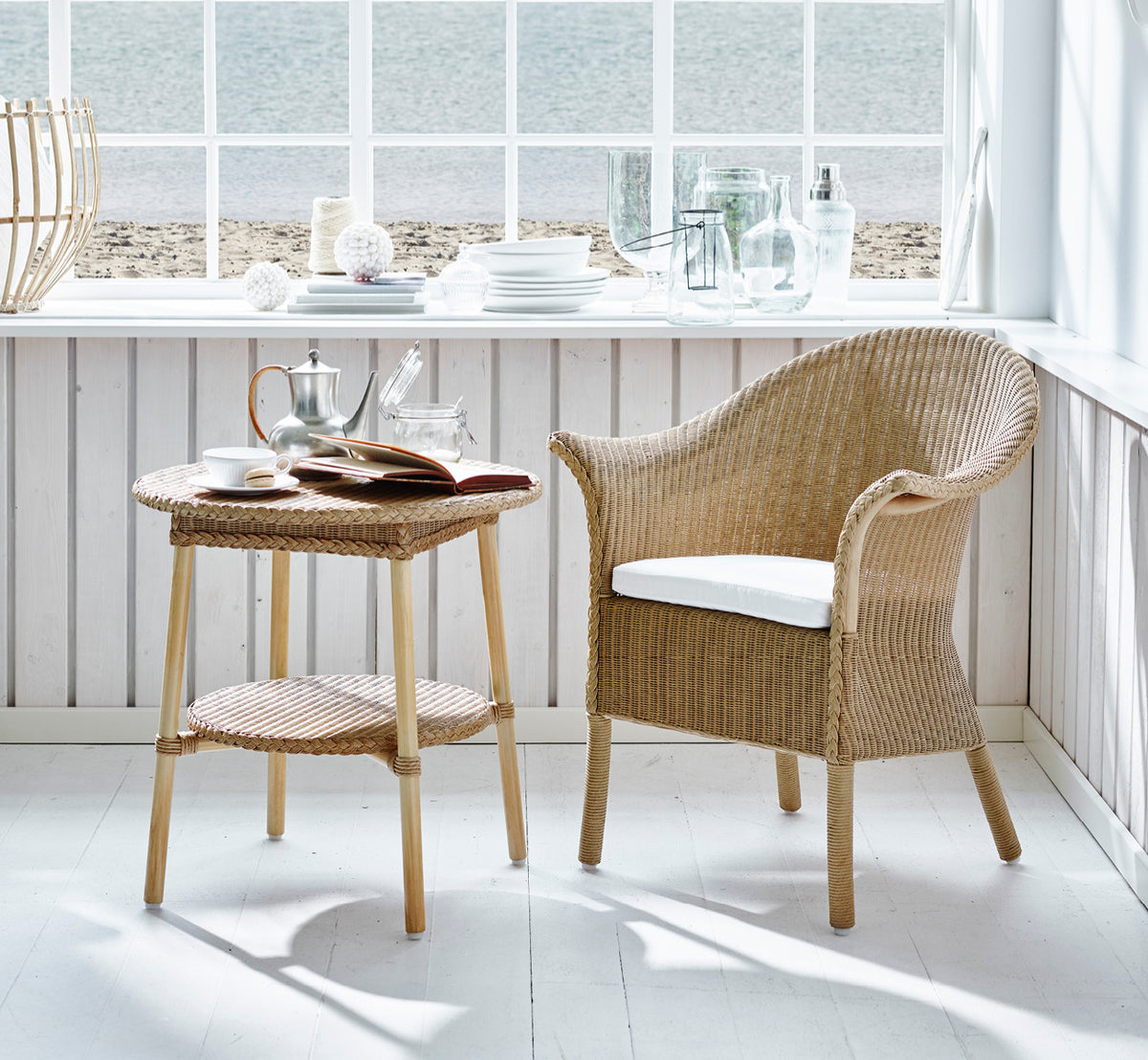 Dies ist ein Lifestyle-Bild von Classic Esszimmerstuhl in natural Loom Rattan Frame, in einem hellen Interieur mit weißen Wandpaneelen und.