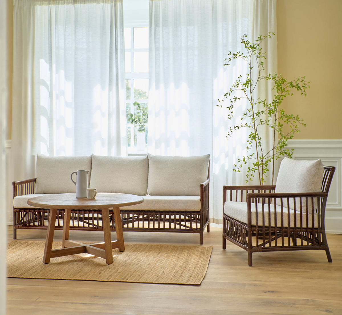 Dies ist ein Lifestyle-Bild von Caroline Sofa in brown rattan. Mit Lounge-Sessel und Teak-Couchtisch auf einem Juteteppich.