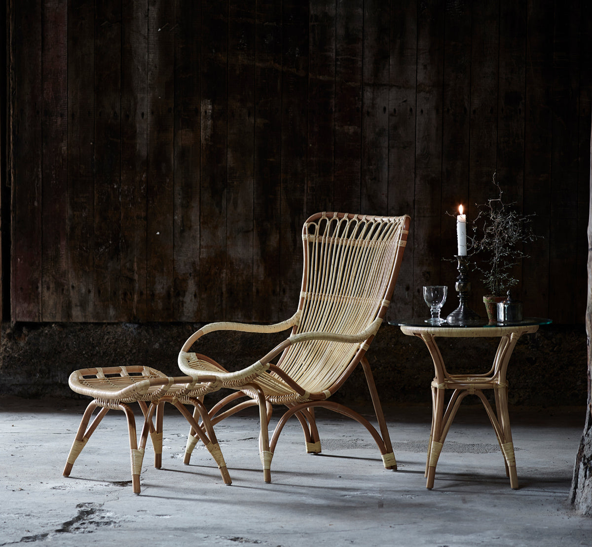 Dies ist ein Lifestyle-Bild von Tony Beistelltisch in natural rattan. Paired with a high-back lounge chair against a dark wood wall.