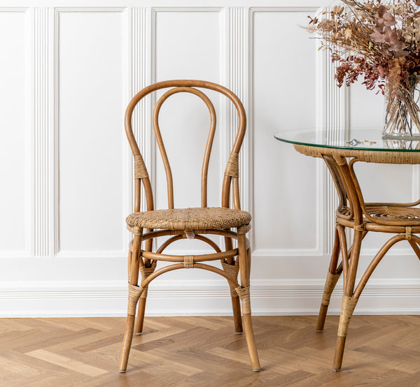 Dies ist ein Lifestyle-Bild von Tony Cafétisch in antique rattan. Mit einem Esszimmerstuhl neben Trockenblumen in einem weiß vertäfelten Interieur kombiniert.