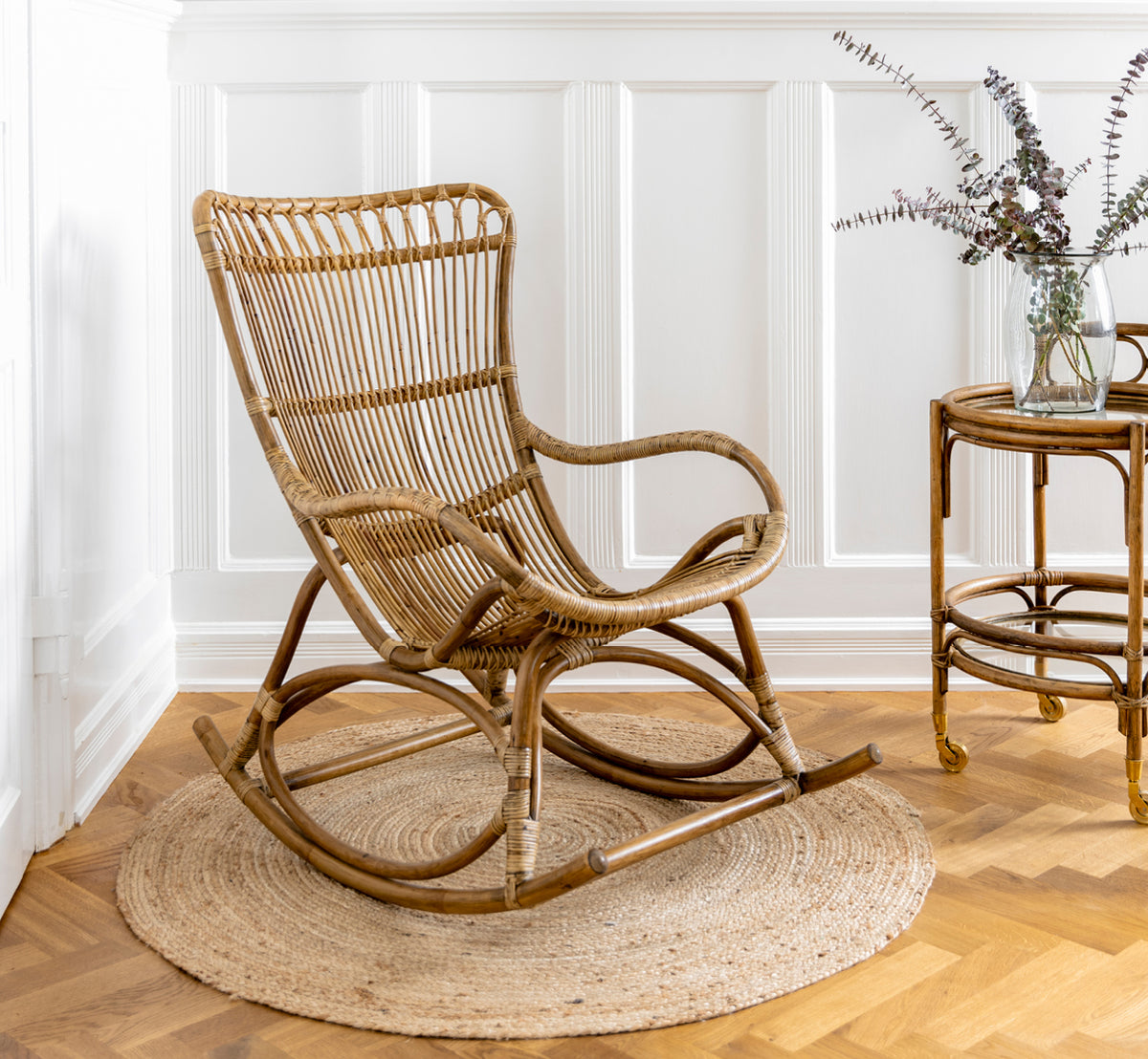 Dies ist ein Lifestyle-Bild von Romeo Servierwagen in antique rattan. Mit Hortensien und Keramik vor einer weißen Backsteinwand gestylt.