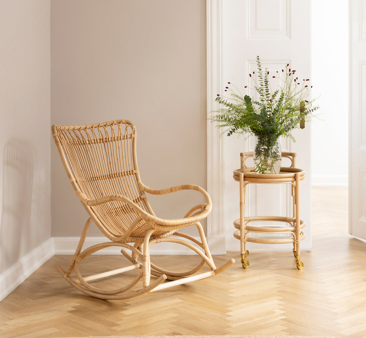 Dies ist ein Lifestyle-Bild von Romeo Trolley i natural rattan. Gestylt mit Gläsern in einer gemütlichen Ecke mit Fischgrätparkett.