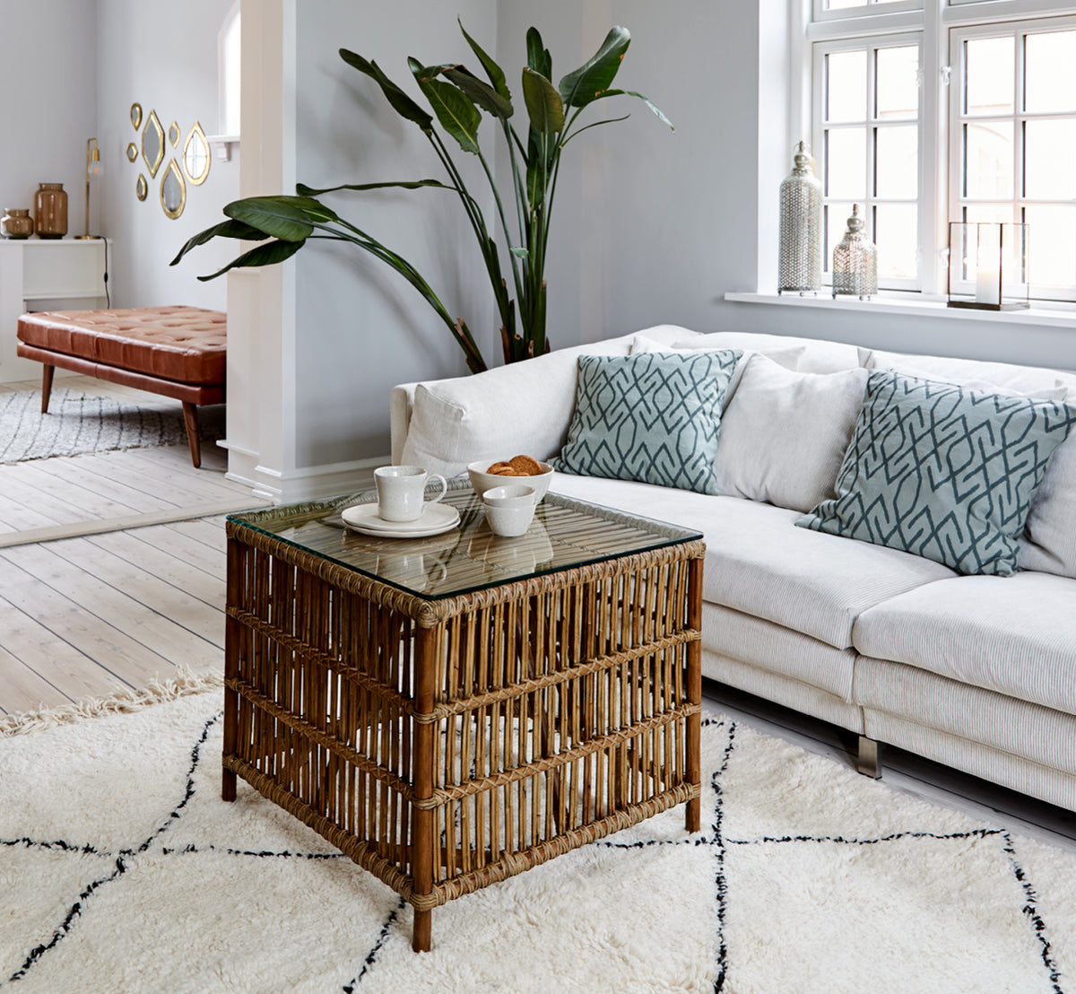 Dies ist ein Lifestyle-Bild von Donatello Beistelltisch in antique rattan, in einem hellen Interieur mit weißen Wandpaneelen und Fischgrätparkett.