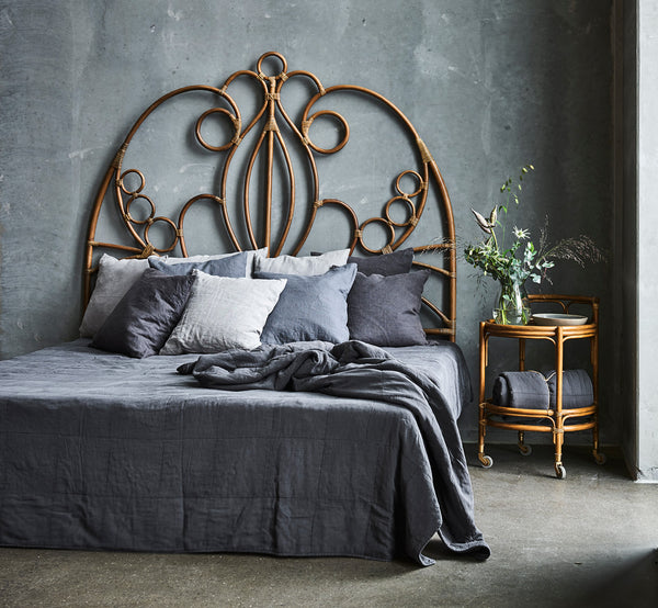 Dies ist ein Lifestyle-Bild von Natalia Kopfteil in antique rattan, in einem ruhigen hellen Schlafzimmer mit neutralem Leinen und Fischgrätparkett.