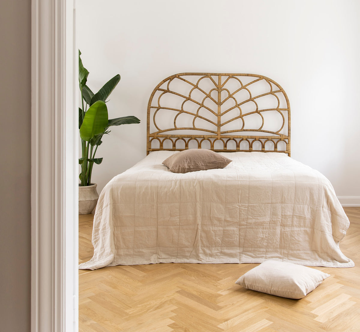 Dies ist ein Lifestyle-Bild von Celia Kopfteil in antique rattan, in einem ruhigen hellen Schlafzimmer mit neutralem Leinen und Fischgrätparkett.