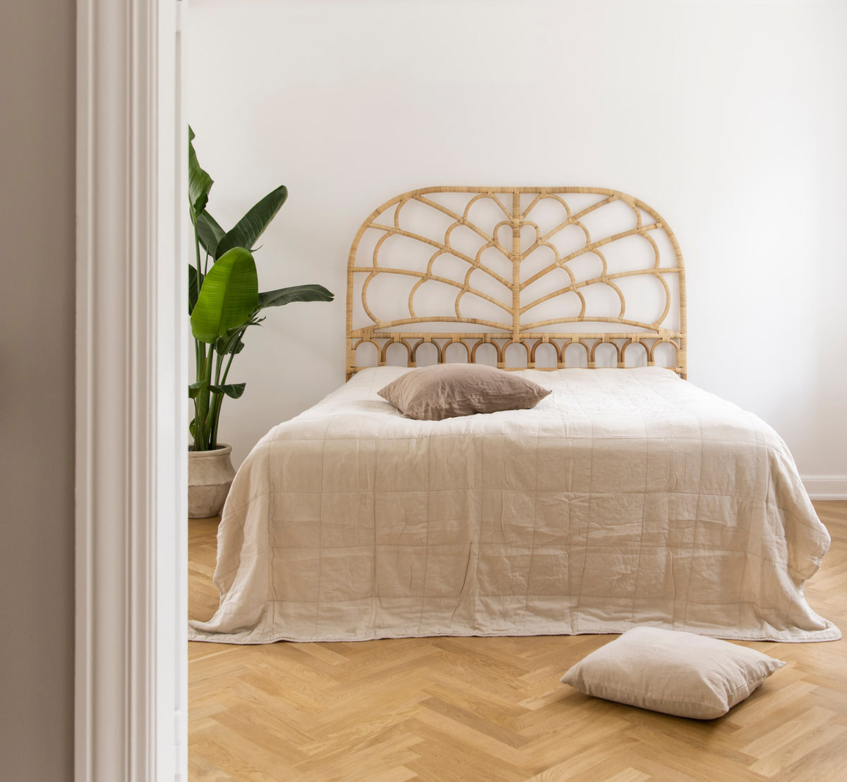 Dies ist ein Lifestyle-Bild von Celia Kopfteil in natural rattan, in einem ruhigen hellen Schlafzimmer mit neutralem Leinen und Fischgrätparkett.