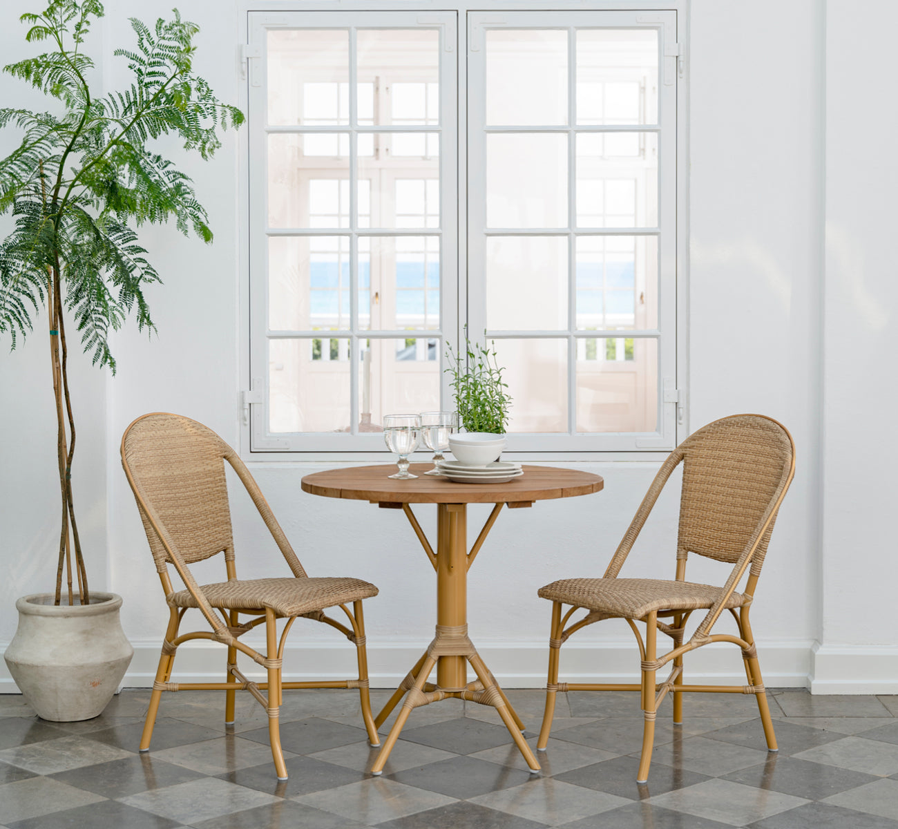 Dies ist ein Lifestyle-Bild von Sofie Exterior Dining Chair i almond aluminium frame natural ArtFibre. Um einen Teak-Außentisch angeordnet.