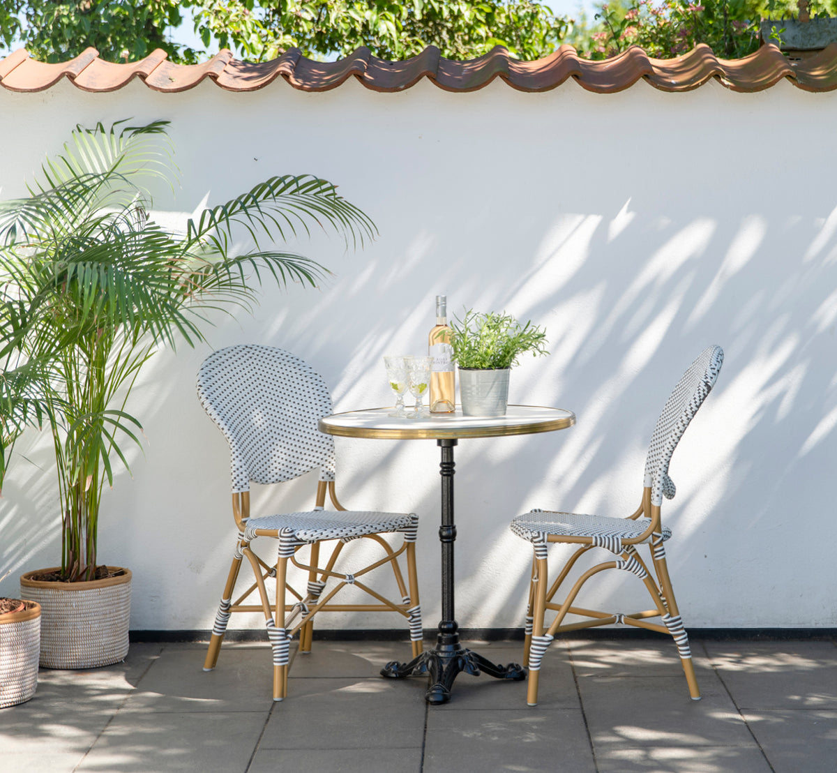 Dies ist ein Lifestyle-Bild von Isabell in almond aluminium frame White w cappuccino dot ArtFibre, auf einer üppigen Gartenterrasse mit Steinboden.
