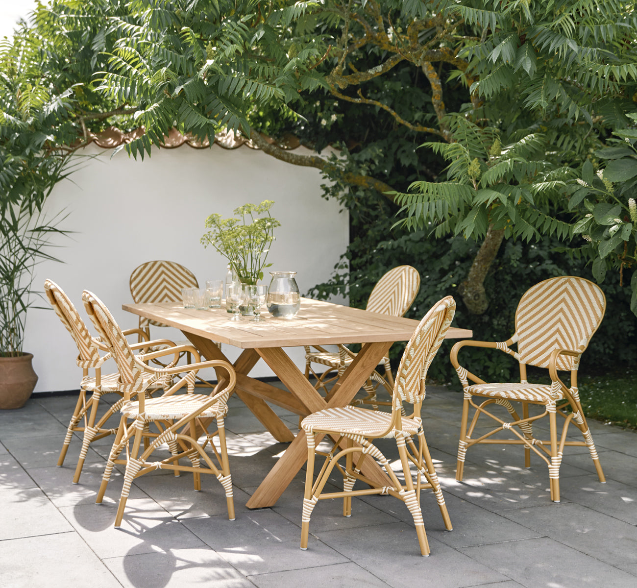Dies ist ein Lifestyle-Bild von Isabell in almond aluminium frame Chevron Honey Ivory ArtFibre, auf einer üppigen Gartenterrasse mit Steinboden und.