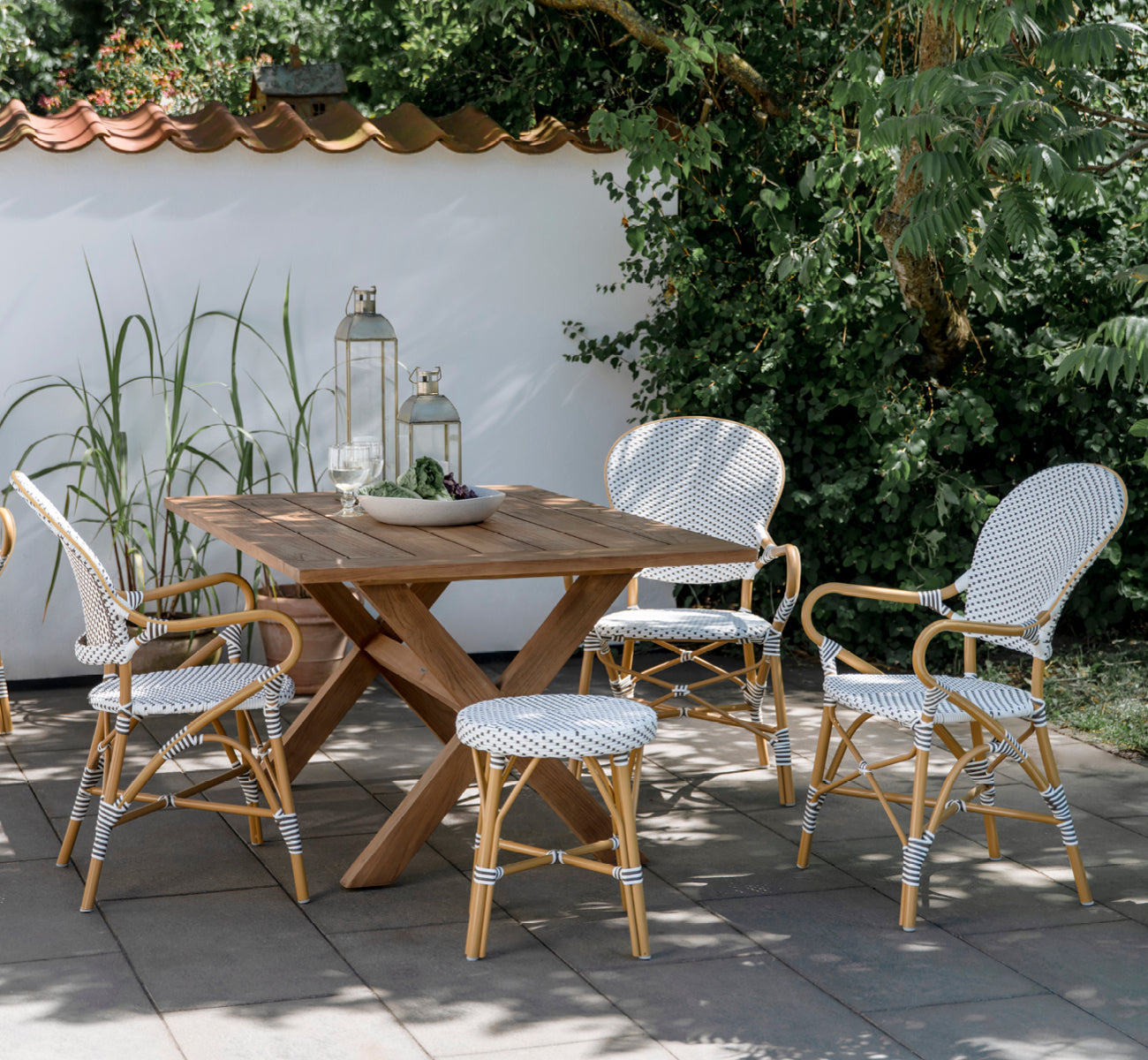 Dies ist ein Lifestyle-Bild von Isabell in almond aluminium frame White w cappuccino dot ArtFibre, auf einer üppigen Gartenterrasse mit Steinboden.