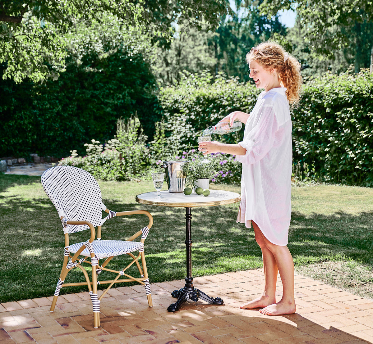 Dies ist ein Lifestyle-Bild von Isabell in almond aluminium frame White w cappuccino dot ArtFibre, auf einer üppigen Gartenterrasse mit Steinboden.