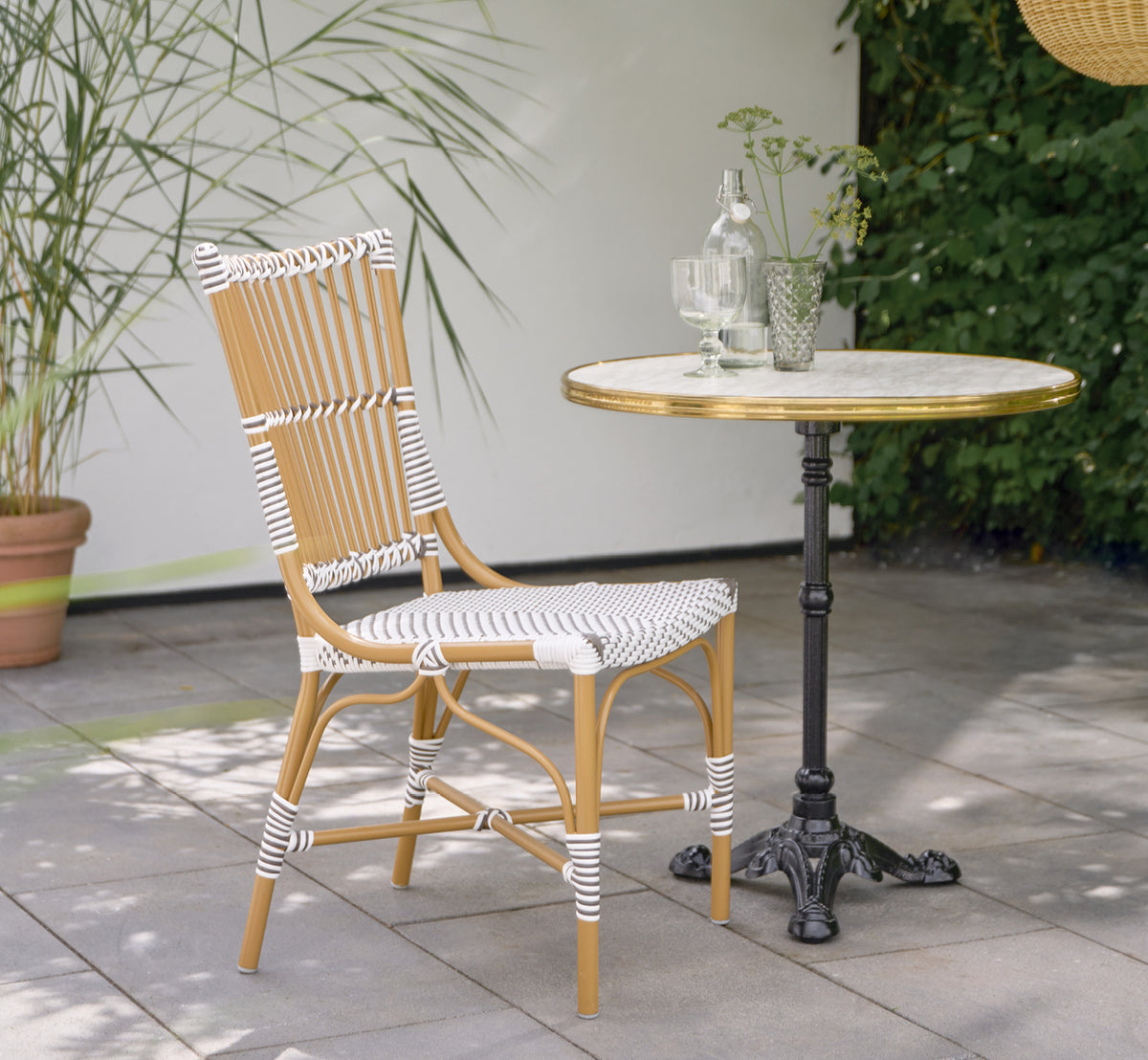 Dies ist ein Lifestyle-Bild von Monique Exterior Dining Chair i white w cappuccino dot ArtFibre. Auf einer sonnigen Terrasse mit Palmen.