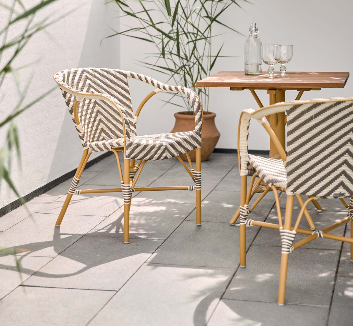Dies ist ein Lifestyle-Bild von Madeleine Außen-Esszimmerstuhl in almond aluminum frame chevron cappuccino ivory ArtFibre. Sonnige Terrasse mit Teaktisch.