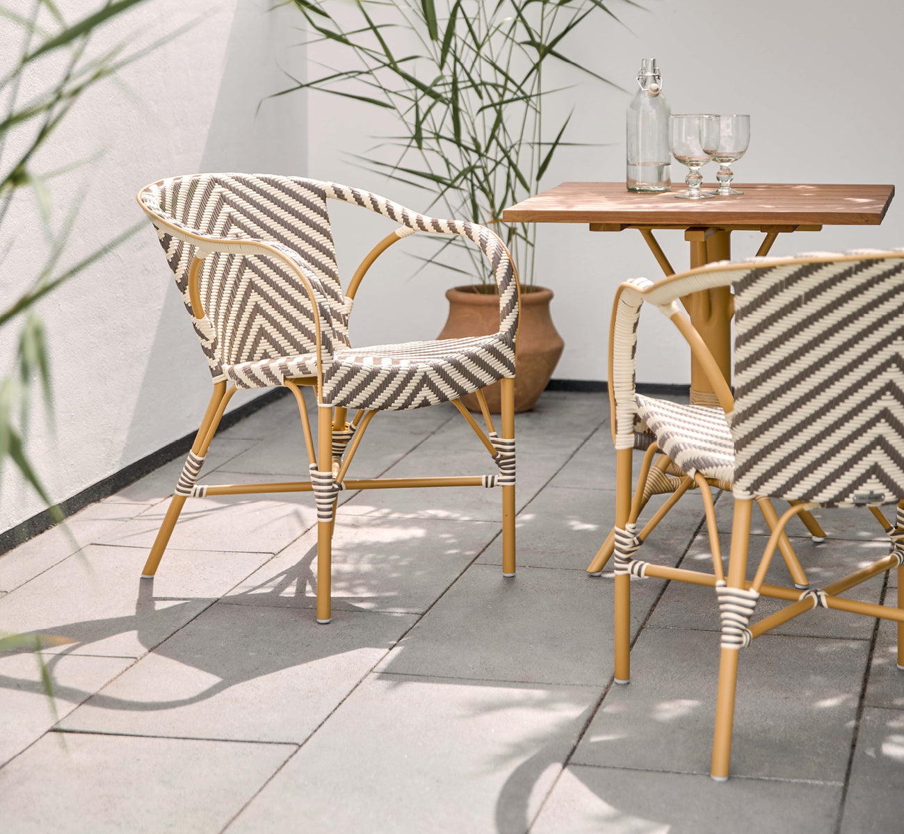 Dies ist ein Lifestyle-Bild von Madeleine Außen-Esszimmerstuhl in almond aluminum frame chevron cappuccino ivory ArtFibre. Sonnige Terrasse mit Teaktisch.