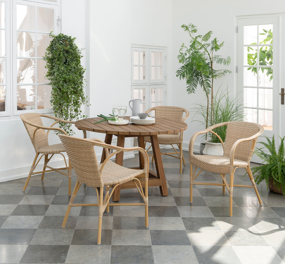 Dies ist ein Lifestyle-Bild von Madeleine Außen-Esszimmerstuhl in almond aluminium frame natural ArtFibre. Heller Wintergarten mit Pflanzen und Fliesenboden.