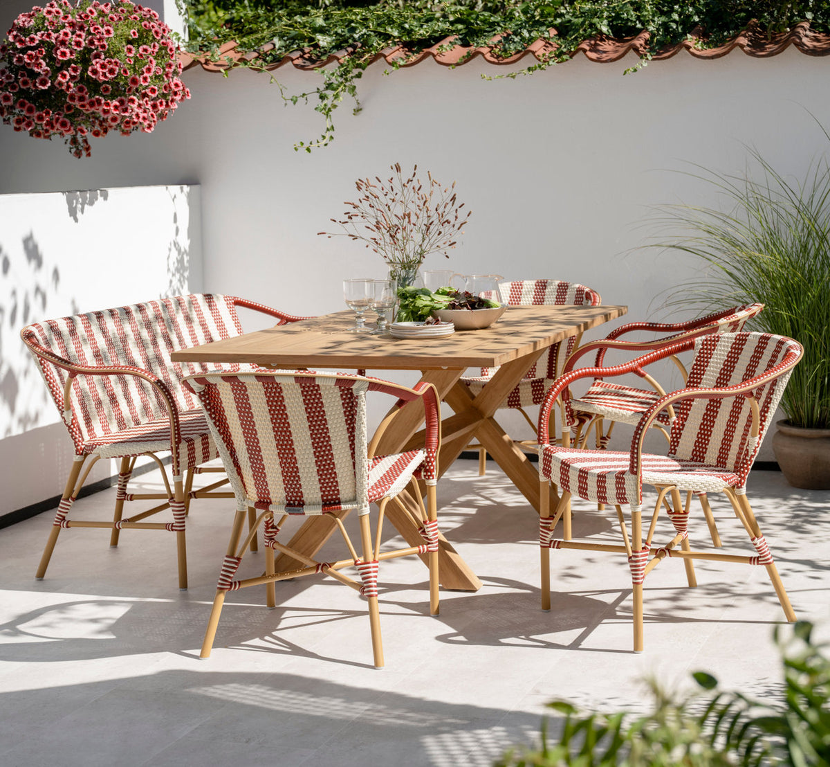 Dies ist ein Lifestyle-Bild von Madeleine Außen-Esszimmerstuhl in almond aluminum frame striped ivory burgundy. An einem Teaktisch auf einer sonnigen Terrasse.