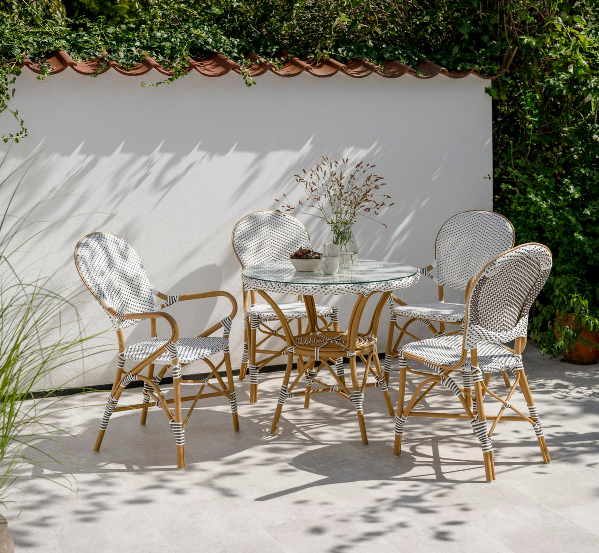 Dies ist ein Lifestyle-Bild von Danielle Außen-Cafétisch in almond aluminium frame white w cappuccino dot artfibre. Mit Stühlen auf einer sonnigen Terrasse.