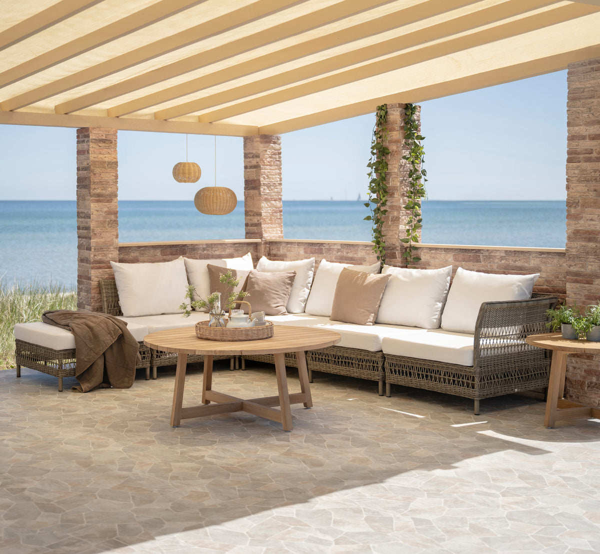 Dies ist ein Lifestyle-Bild von Mona Außen-Modulsofa-Corner Module in antique grey artfibre aluminium. Unter einer Pergola am Meer.