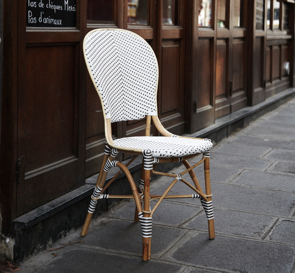 Dies ist ein Lifestyle-Bild von Isabell in white w cappuccino dot ArtFibre Skin on Rattan frame, auf einer hellen Küstenterrasse mit Meerblick und.