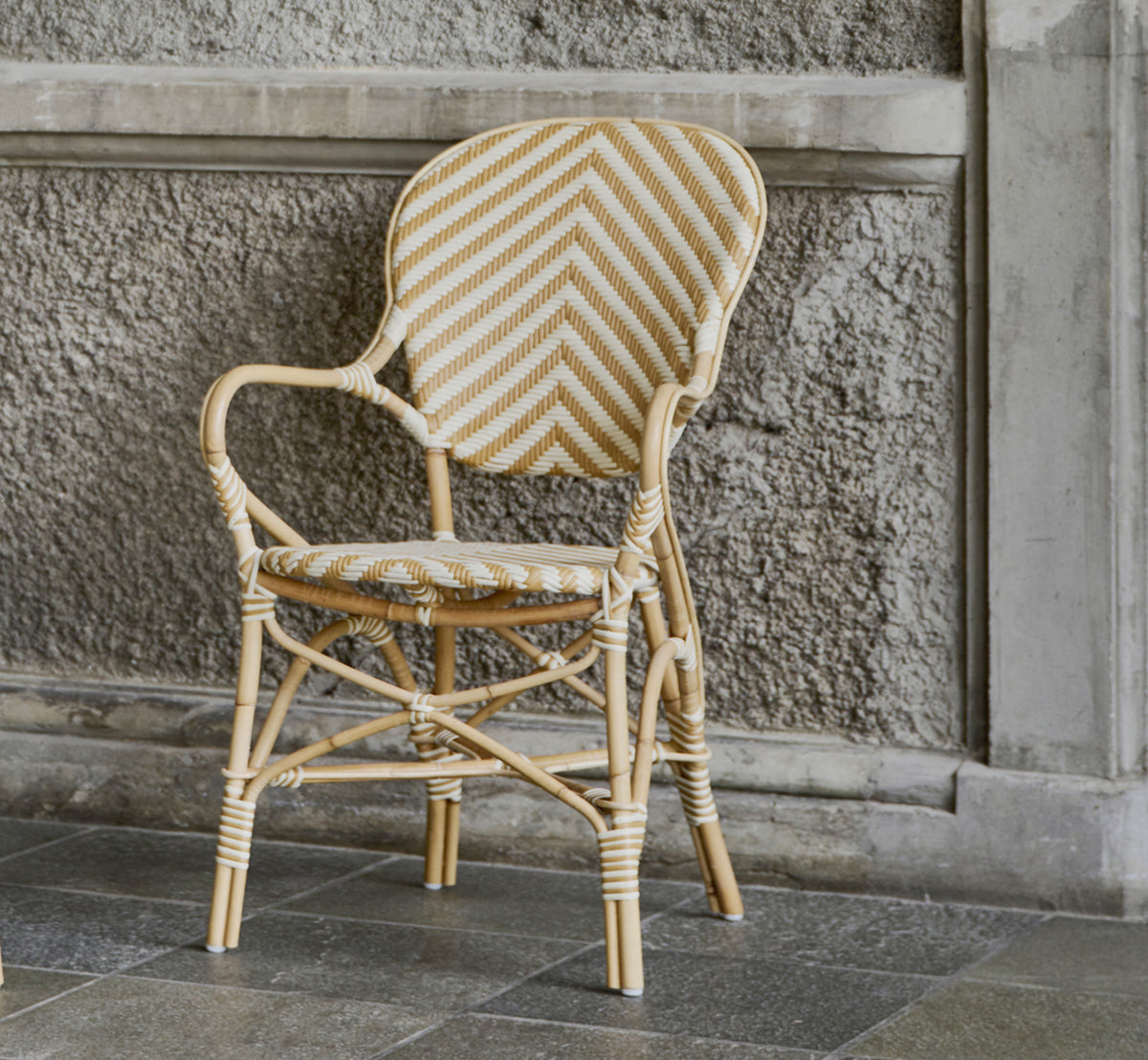 Dies ist ein Lifestyle-Bild von Isabell Esszimmer-Armlehnstuhl in chevron Honey Ivory ArtFibre Skin on Rattan frame, in einem hellen Essbereich mit.