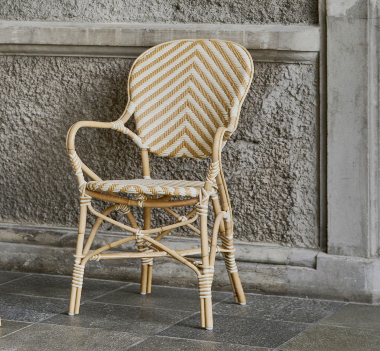 Dies ist ein Lifestyle-Bild von Isabell Esszimmer-Armlehnstuhl in chevron Honey Ivory ArtFibre Skin on Rattan frame, in einem hellen Essbereich mit.