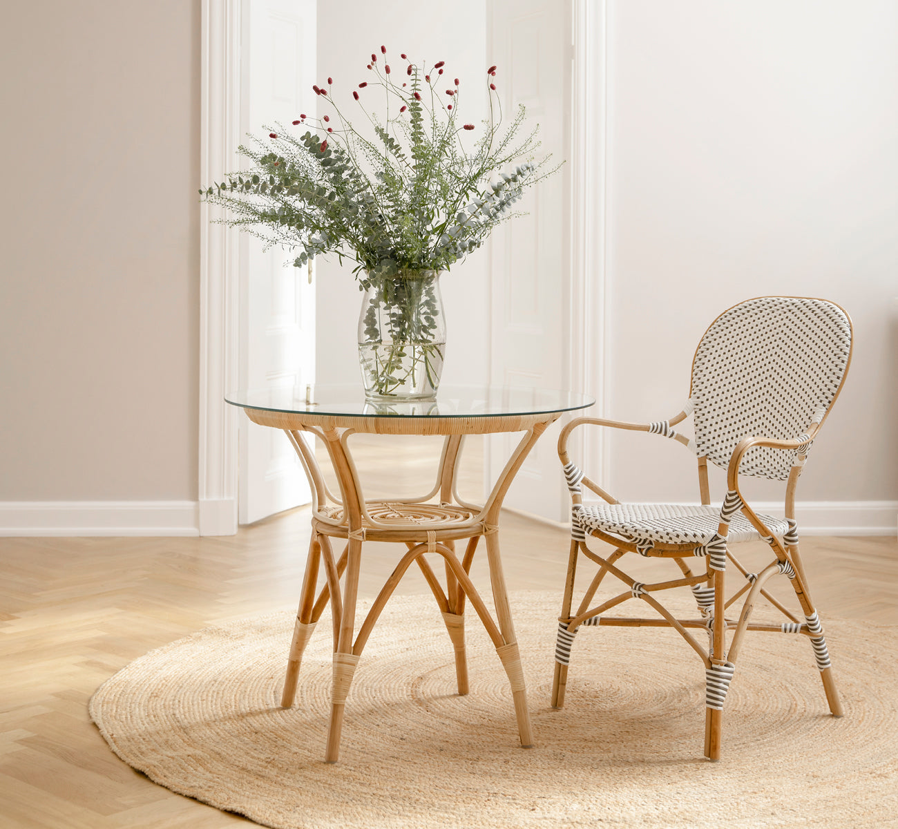 Dies ist ein Lifestyle-Bild von Isabell Esszimmer-Armlehnstuhl in white w cappuccino dot ArtFibre Skin on Rattan frame, in einem hellen Essbereich.