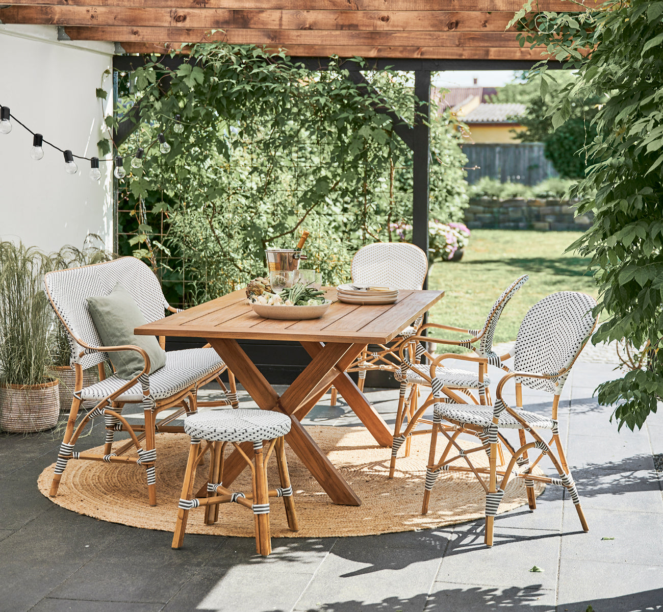 Dies ist ein Lifestyle-Bild von Simone Hocker in white w cappuccino dot ArtFibre Skin on Rattan frame. An einem Teak-Gartentisch.