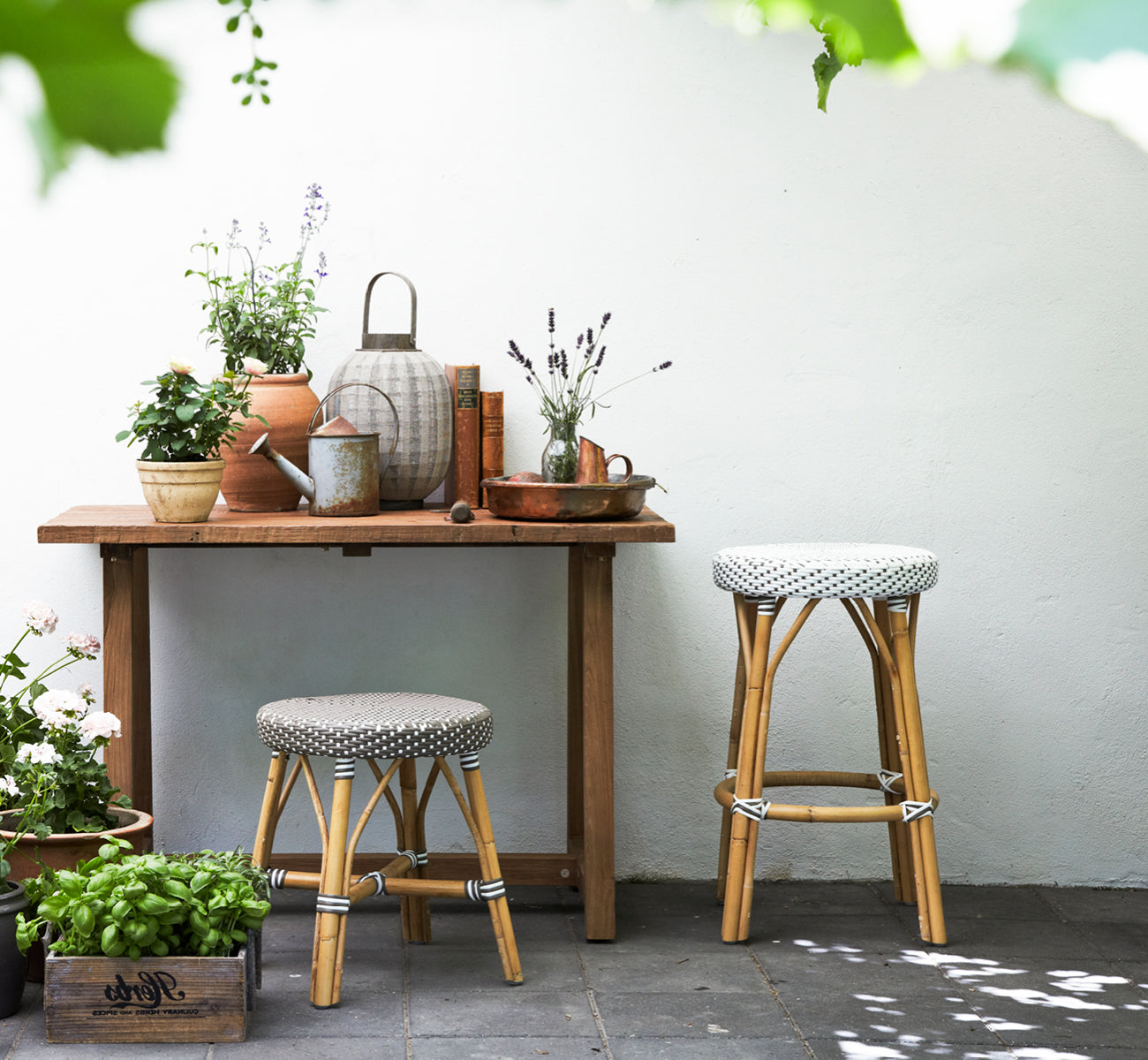 Dies ist ein Lifestyle-Bild von Simone Barstuhl in white w cappuccino dot ArtFibre Skin on Rattan frame. An einem rustikalen Pflanztisch.