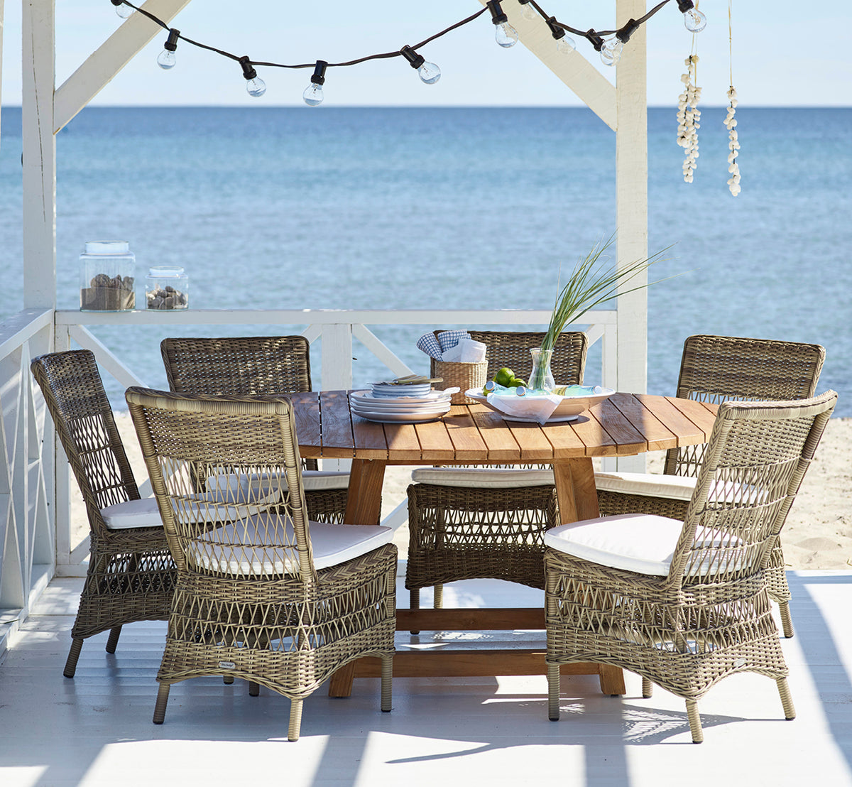 Dies ist ein Lifestyle-Bild von Marie Exterior Side Chair i antique grey artfibre aluminium. In einem Strandpavillon zum Abendessen gedeckt.
