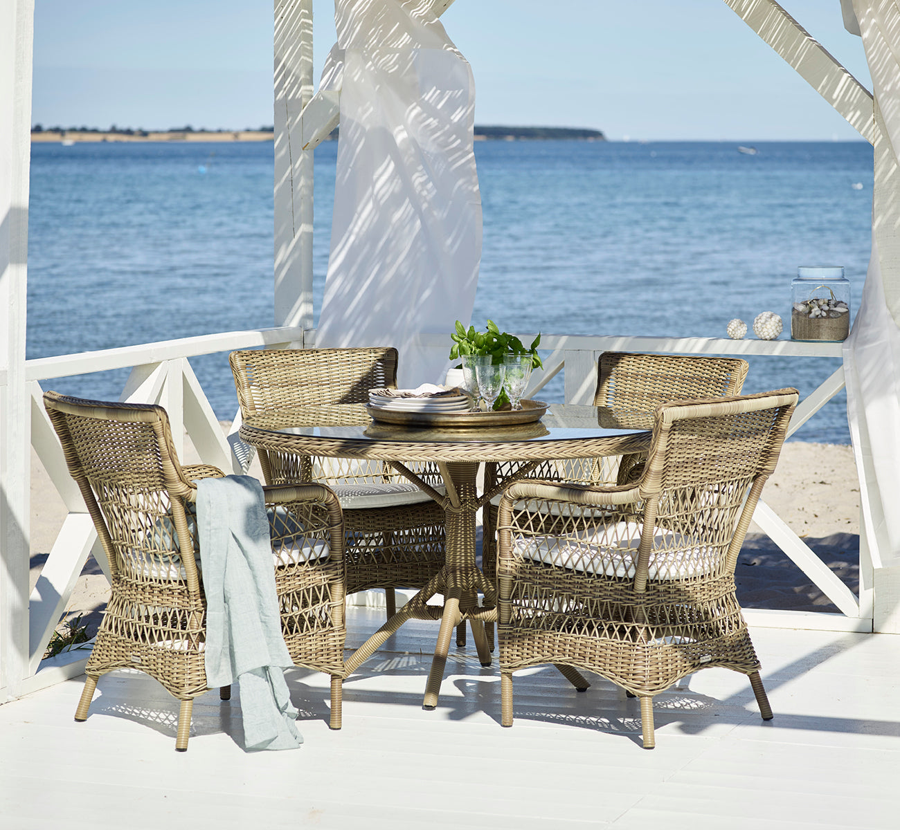 Dies ist ein Lifestyle-Bild von Marie Exterior Armchair i antique grey artfibre aluminium. In einem überdachten Pavillon am Meer.