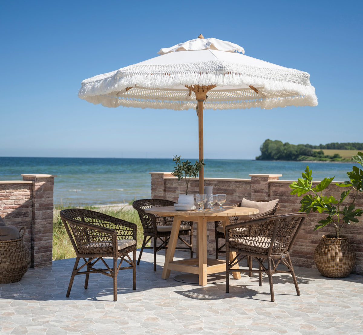 Dies ist ein Lifestyle-Bild von Emma Außenstuhl in brown artfibre aluminum. Zum Mittagessen gedeckt auf einer Terrasse am Meer.