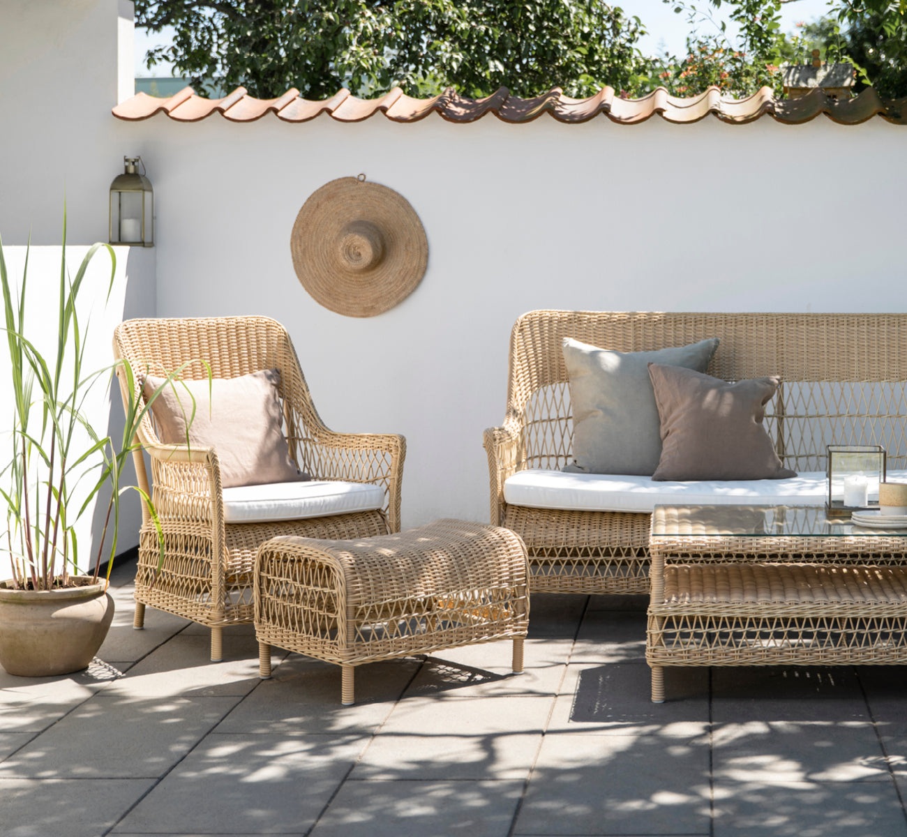 Dies ist ein Lifestyle-Bild von Dawn Lounge-Sessel in natural ArtFibre Aluminium, auf einer Küstenterrasse mit Meerblick, Strandgräsern und weißen.
