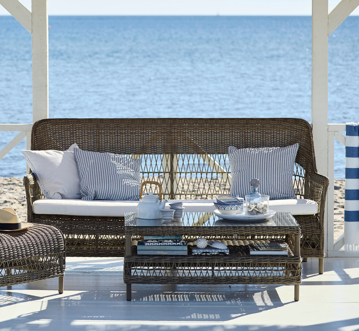Dies ist ein Lifestyle-Bild von Dawn Sofa in antique Grey ArtFibre Aluminium, auf einer Küstenterrasse mit weißem Holzdeck und Meerblick.