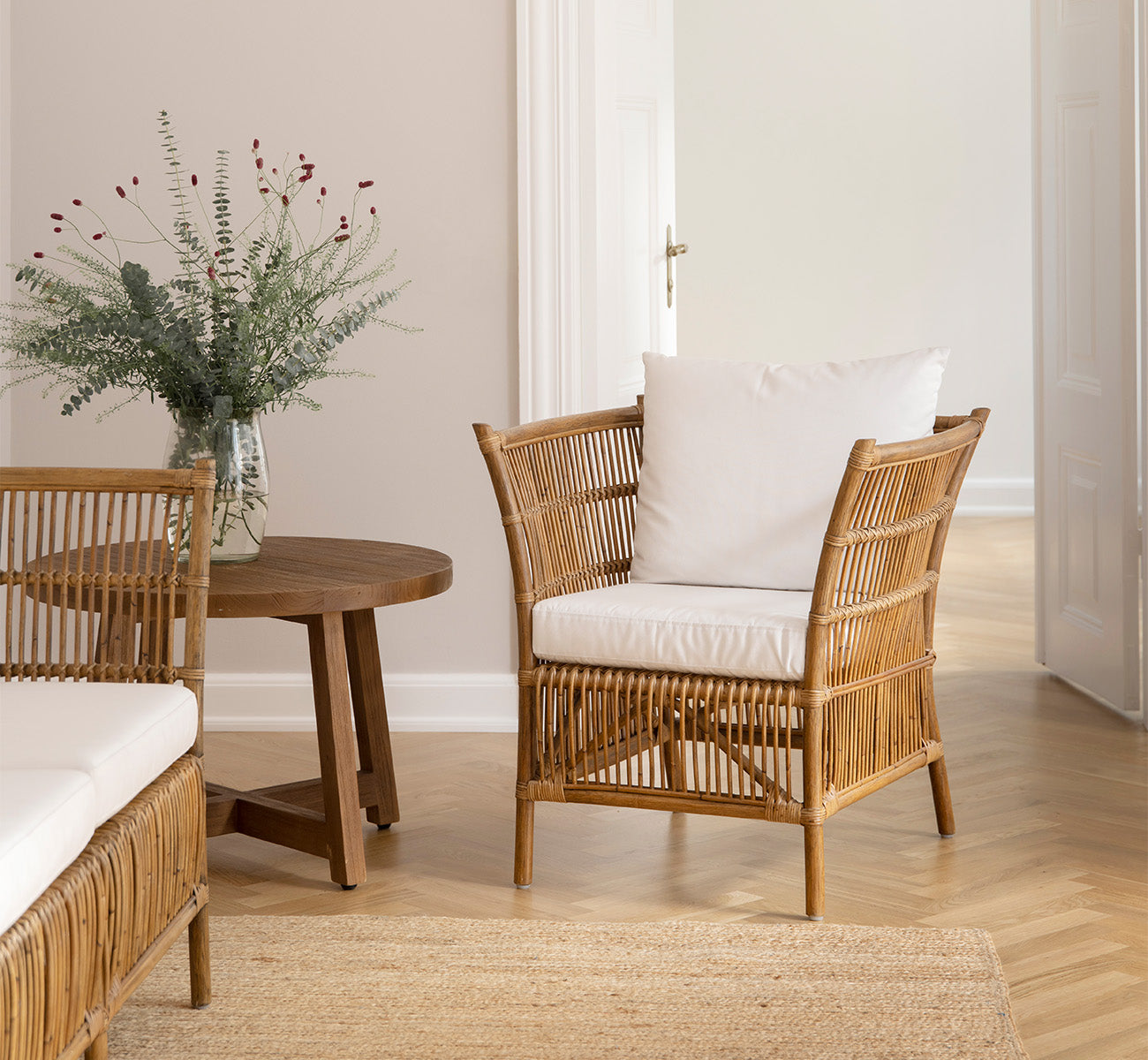 Dies ist ein Lifestyle-Bild von Aksel Couchtisch in teak indoor, in einem hellen Interieur mit Fischgrätparkett und Rattanstühlen.