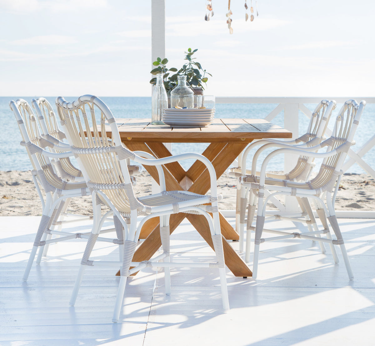 Dies ist ein Lifestyle-Bild von Colonial Tisch 160 in outdoor Teak, auf einer Strandterrasse mit weißem Holzdeck und Meerblick.