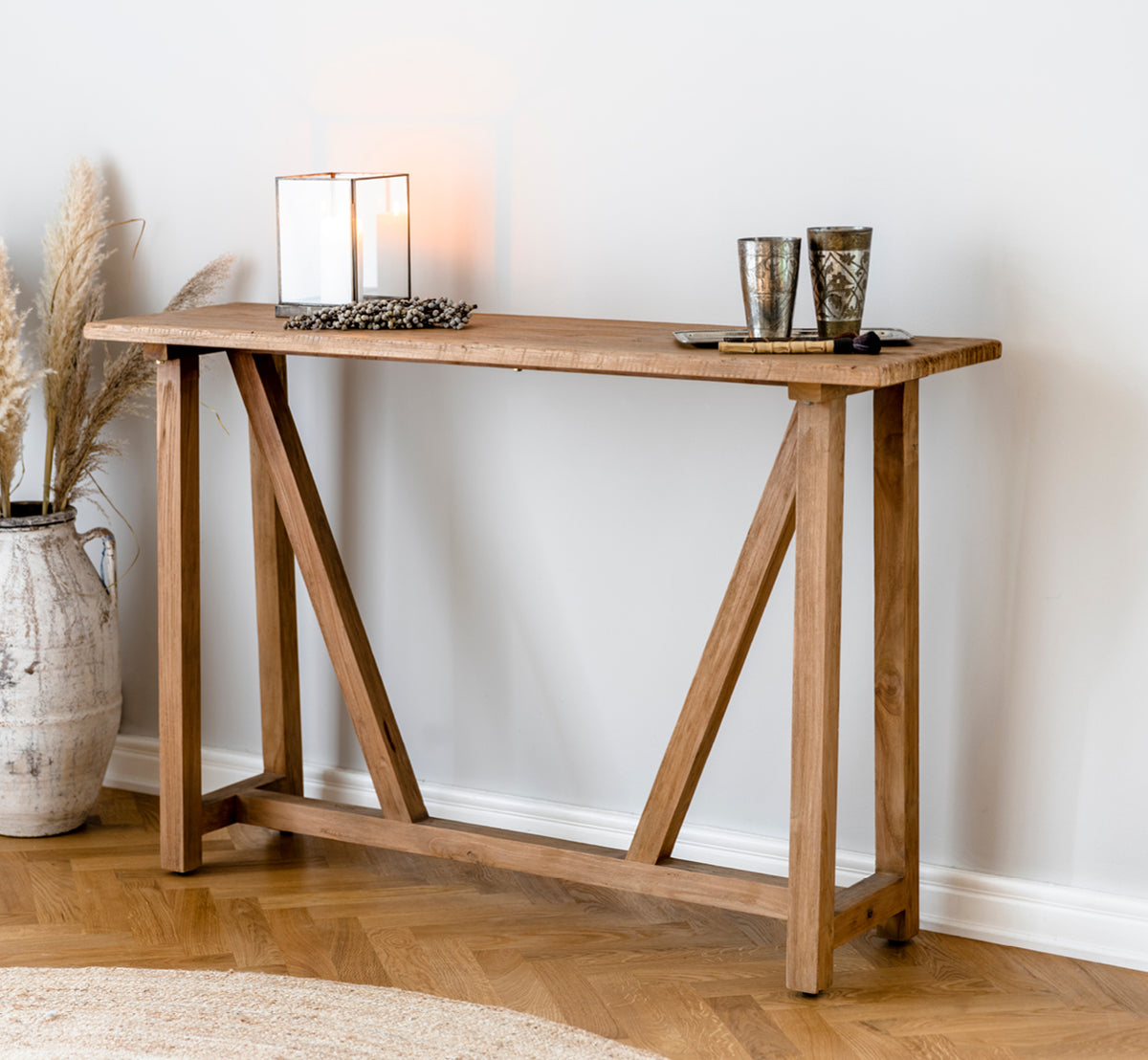 Dies ist ein Lifestyle-Bild von Lucas Teak Konsolentisch in teak indoor. Mit Kerzenhaltern und Pampasgras in einem warmen Ambiente mit Juteteppich gestylt.