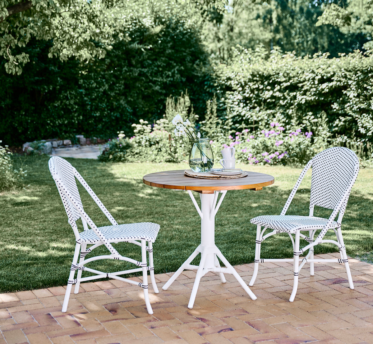Dies ist ein Lifestyle-Bild von Nicole Cafe Table i white aluminium frame white ArtFibre. In einem Strandpavillon mit Piano Armlehnstühlen.