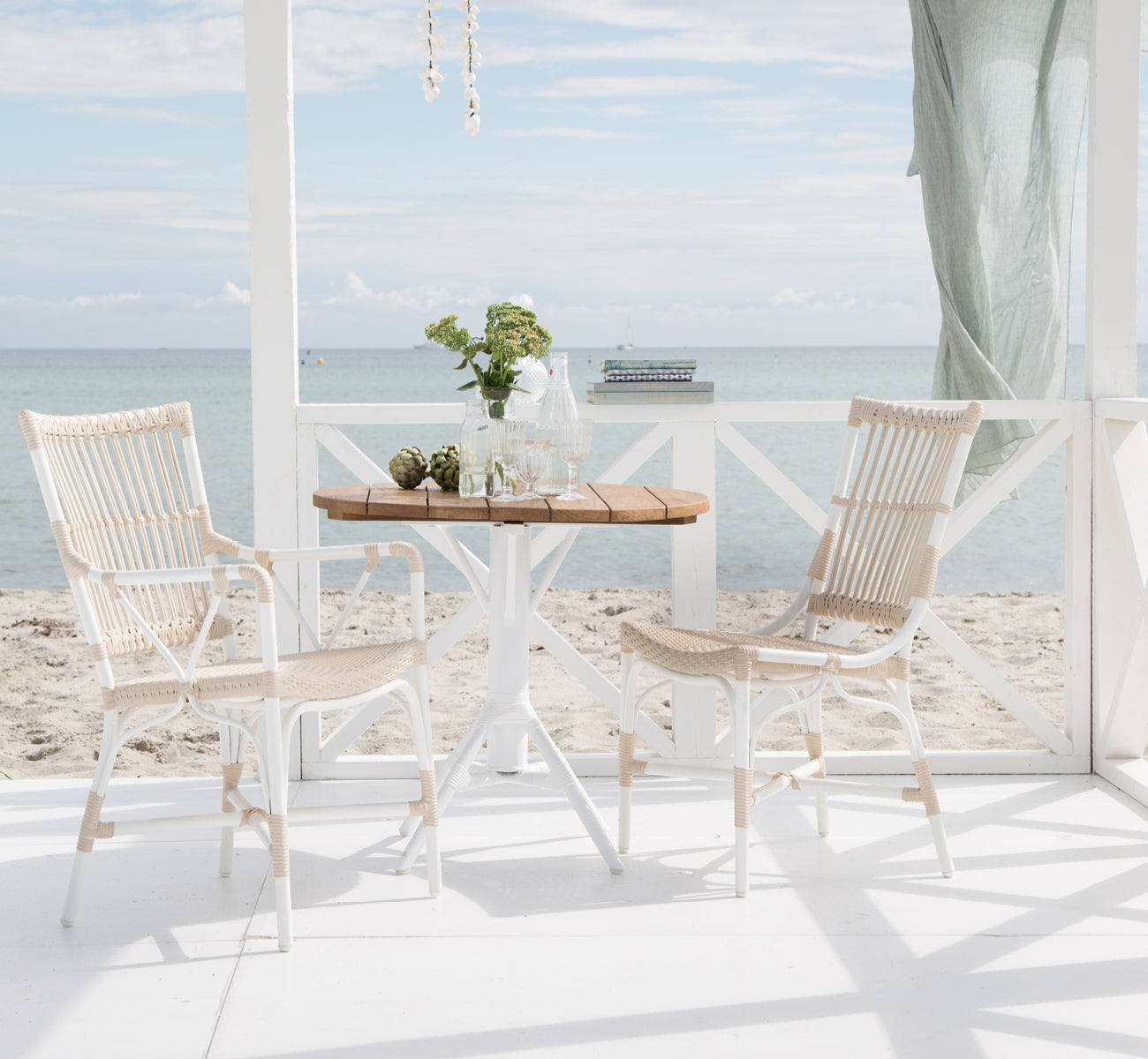 Dies ist ein Lifestyle-Bild von Nicole Cafe Table i white aluminium frame white ArtFibre. Mit Piano-Stühlen auf einem Deck am Meer.