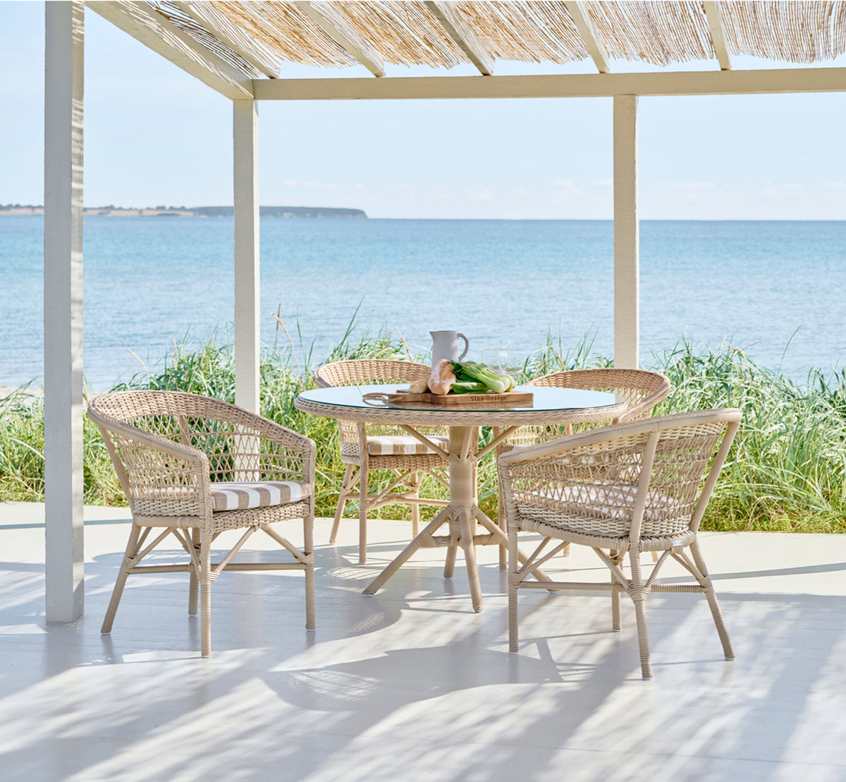 Dies ist ein Lifestyle-Bild von Grace Außen-Esstisch in natural ArtFibre Aluminium, auf einer üppigen Gartenterrasse mit Steinboden und überhängenden.